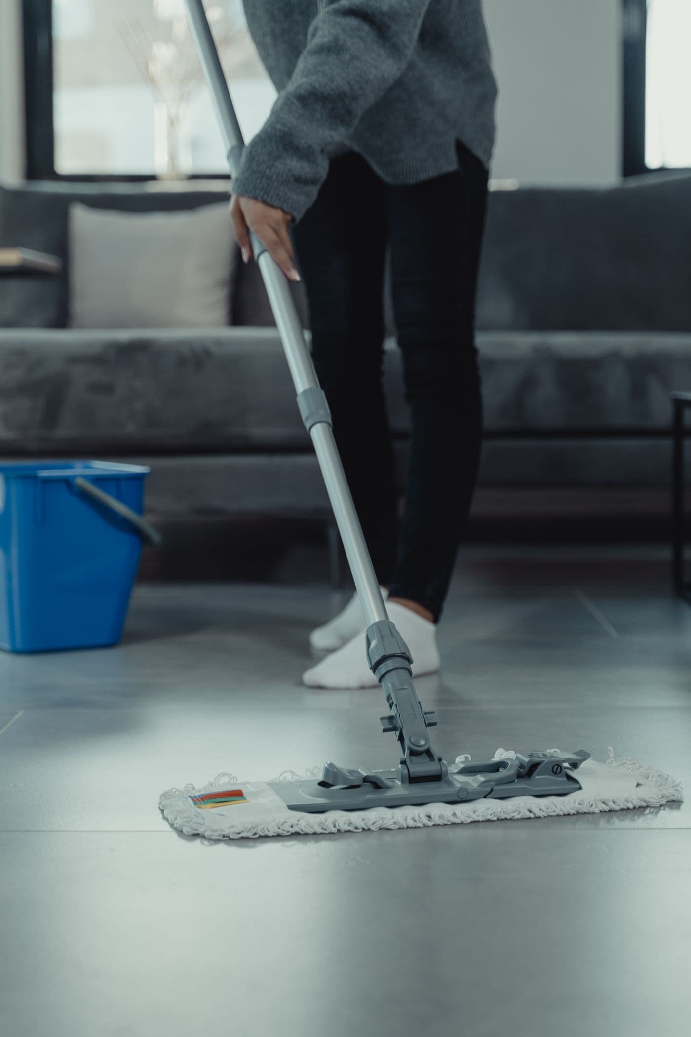 Person wischt mit einem Flachwischer und Putzeimer einen Boden
